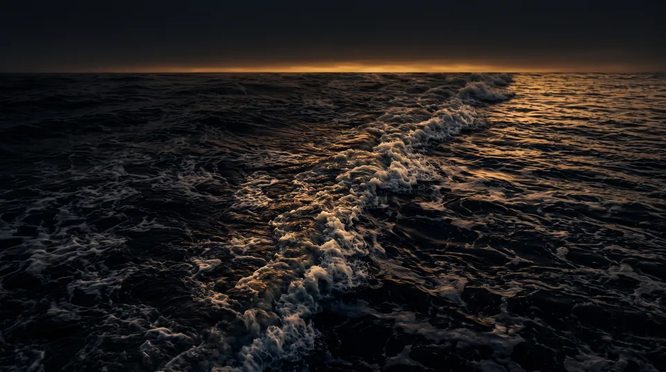 A dark ocean reshaping itself under a band of first light